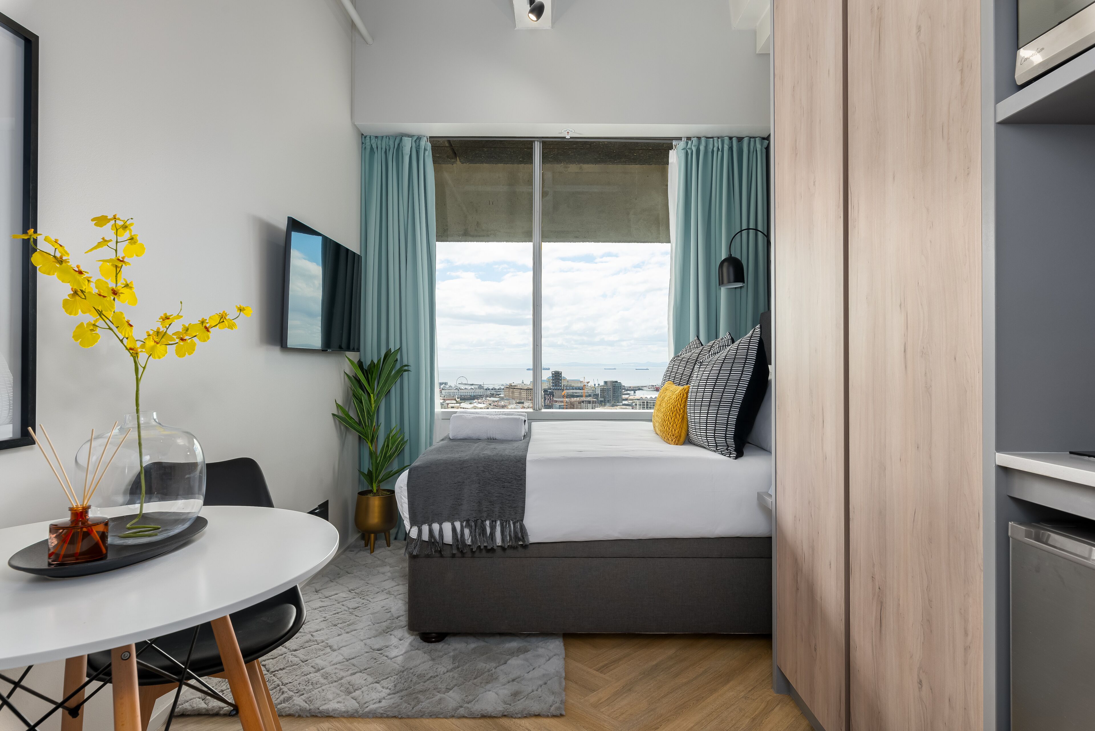 Une chambre moderne avec une grande fenêtre, un lit, une table de chevet, une chaise et une vue sur la ville.