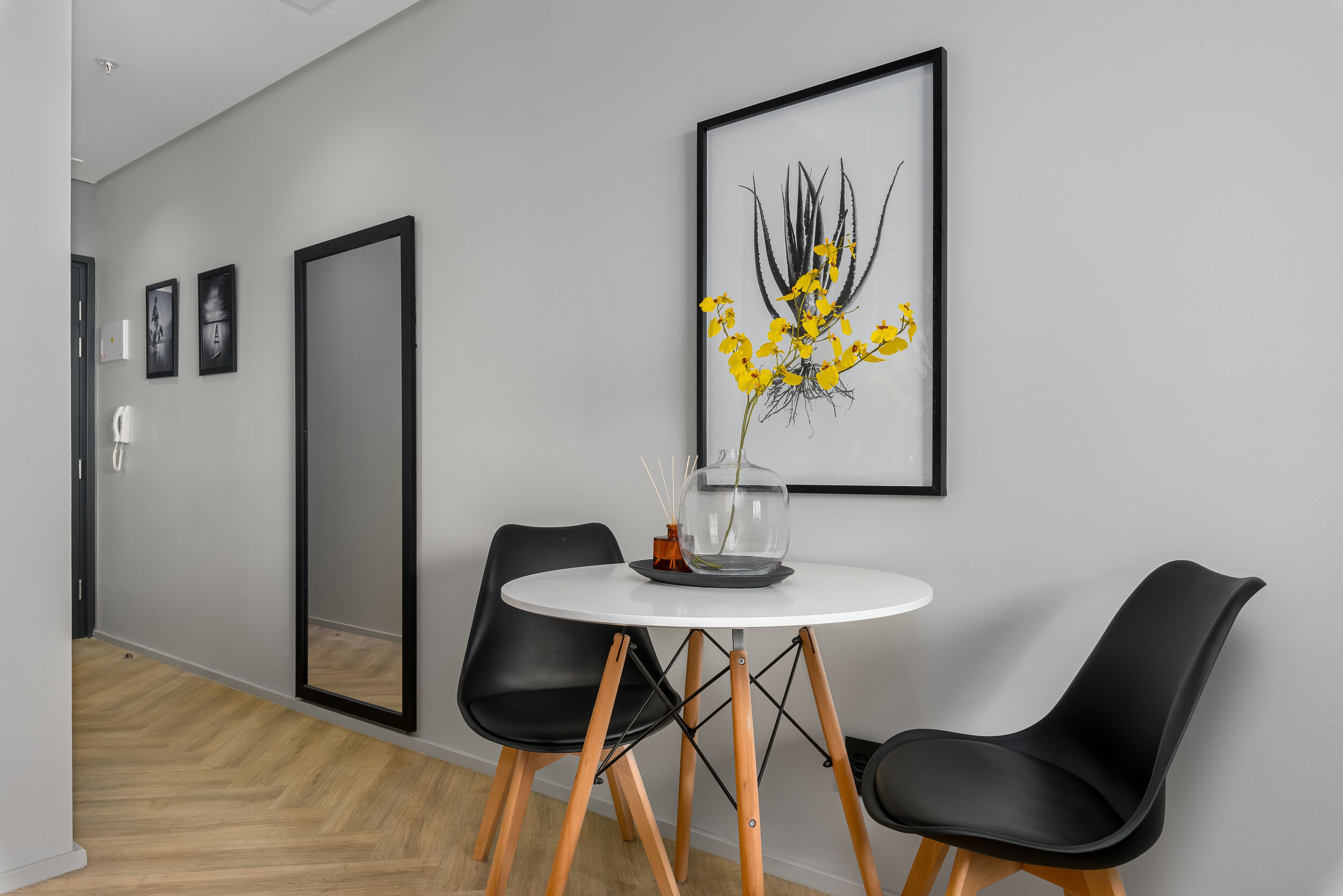 Un comedor moderno con una mesa redonda, dos sillas negras y una obra de arte enmarcada en la pared.