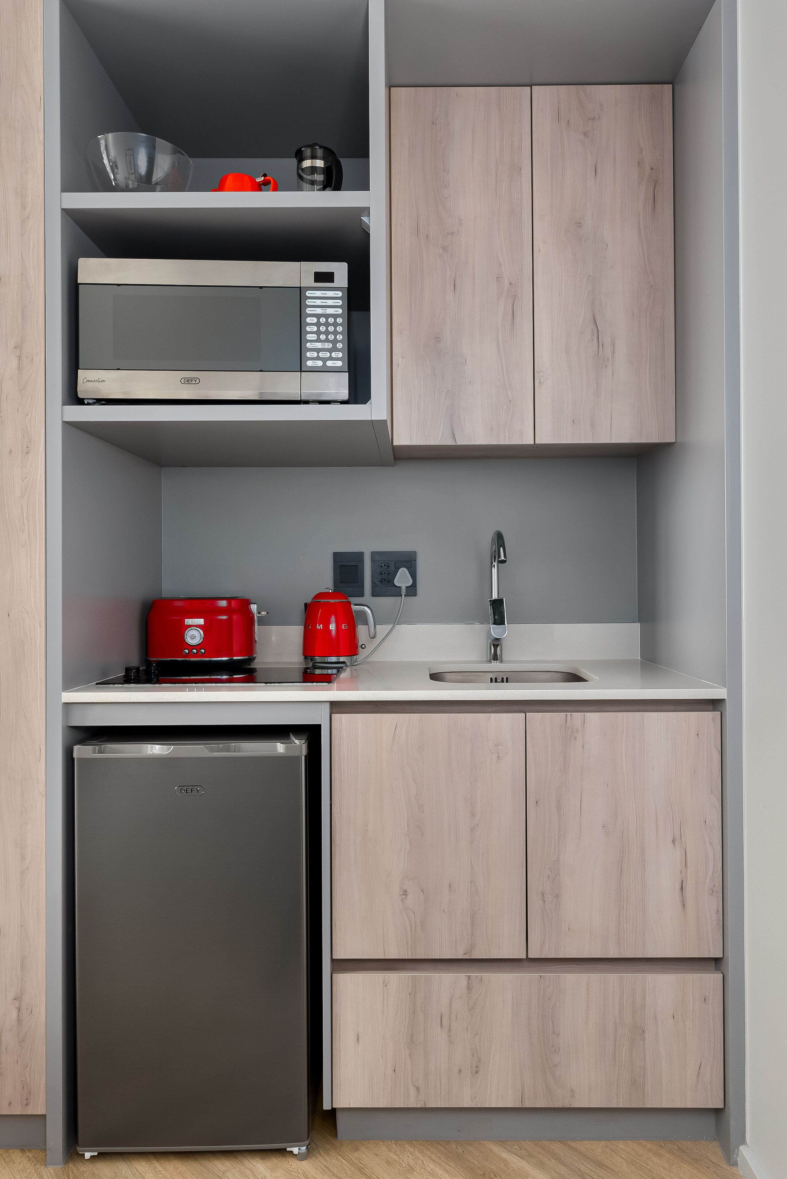 Une cuisine compacte équipée d’un four à micro-ondes, d’une cafetière rouge et d’un petit réfrigérateur.