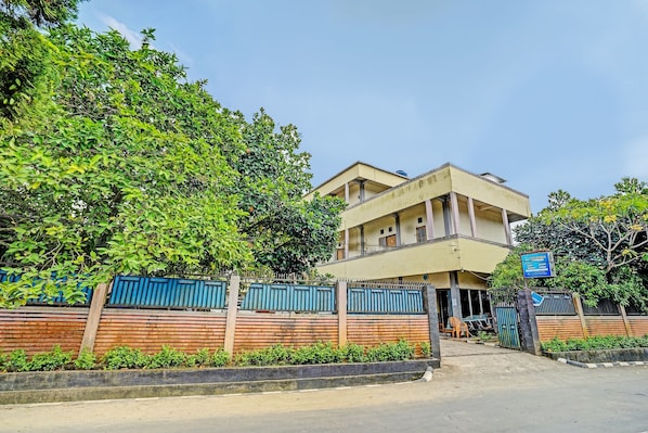 A two-story building with a gated entrance, surrounded by greenery and a blue fence.
