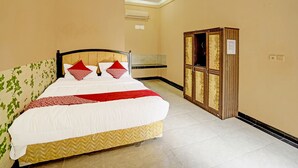 A neatly made bed with a white and red bedspread, a wooden headboard, and two red pillows. A wooden cabinet with glass doors is to the right of the bed. - OYO Life 90508 Wisma Kenanga (Palembang)