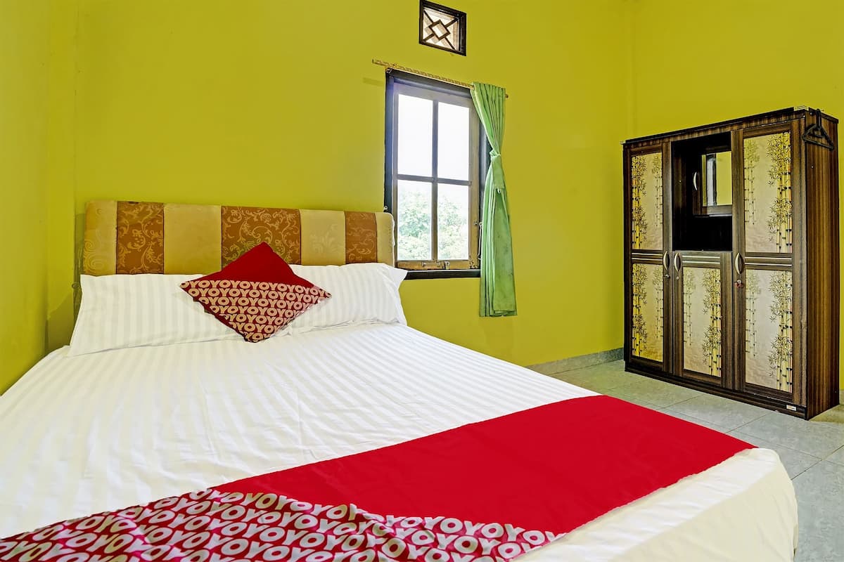 Un lit recouvert d’une couvre-lit rouge et blanche, un oreiller à motifs et une fenêtre ornée d’un rideau vert.