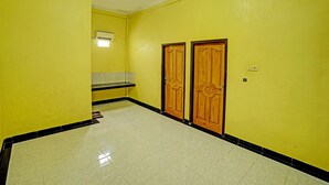 A hallway with yellow walls, a tiled floor, and two wooden doors. - OYO Life 90508 Wisma Kenanga (Palembang)