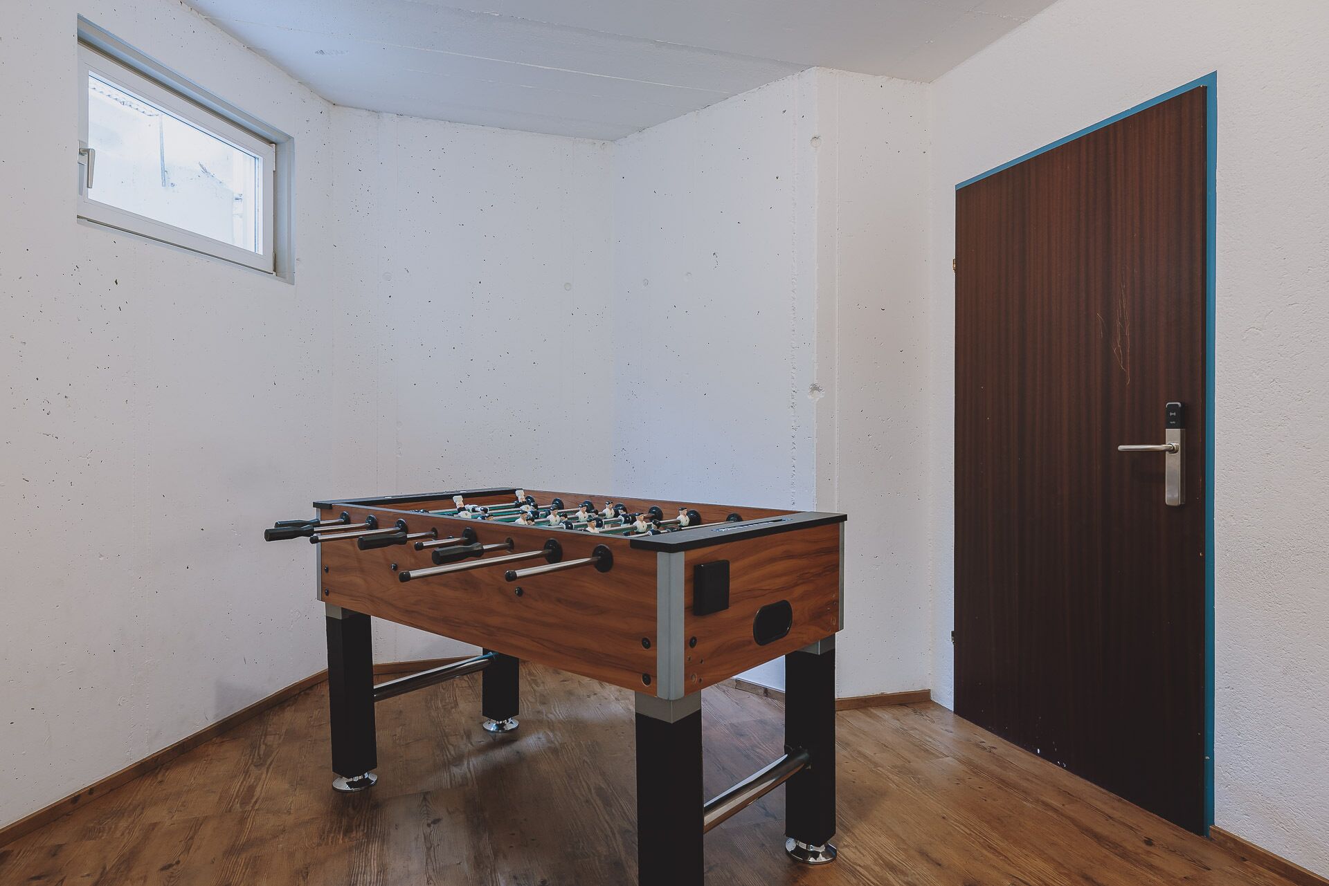 Una habitación con una mesa de fútbolín de madera, una puerta y una ventana.