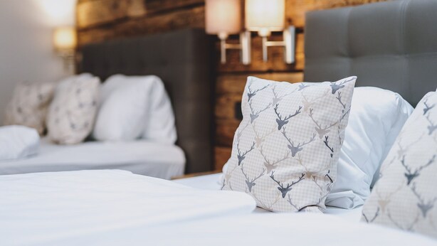 A hotel room with a wooden wall, a bed with white bedding, and a nightstand with lamps. - Chalet Badia by we rent (Zell am See)