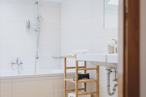A modern bathroom with a bathtub, a shower, a wooden shelf with a towel, and a sink. - Chalet Badia by we rent (Zell am See)