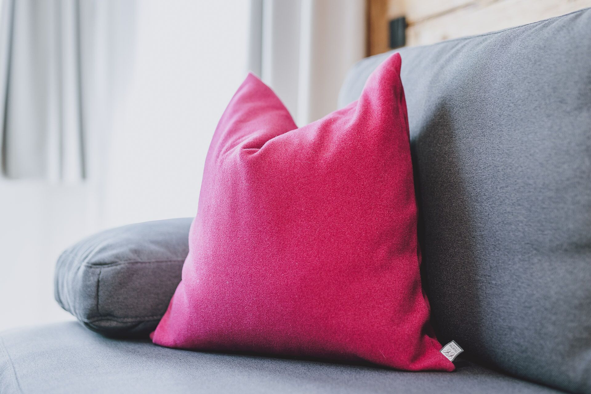A grey sofa with a single pink pillow.