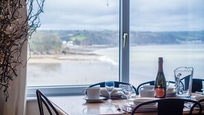 Una mesa de comedor con una botella de vino, una jarrón y vista a una playa a través de un ventanal amplio.