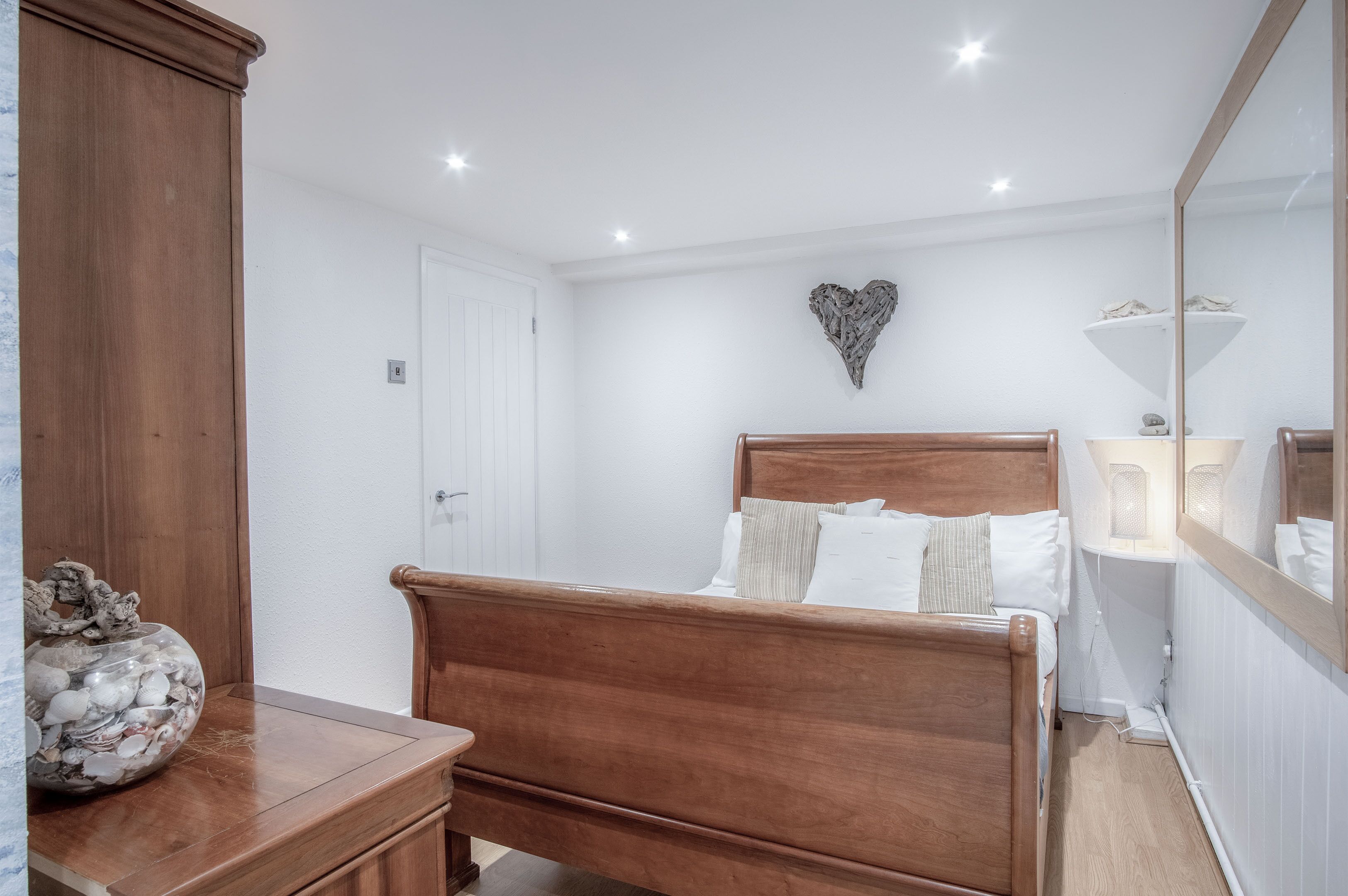 A bedroom with a wooden bed, white walls, a heart-shaped decoration, and a bedside lamp.