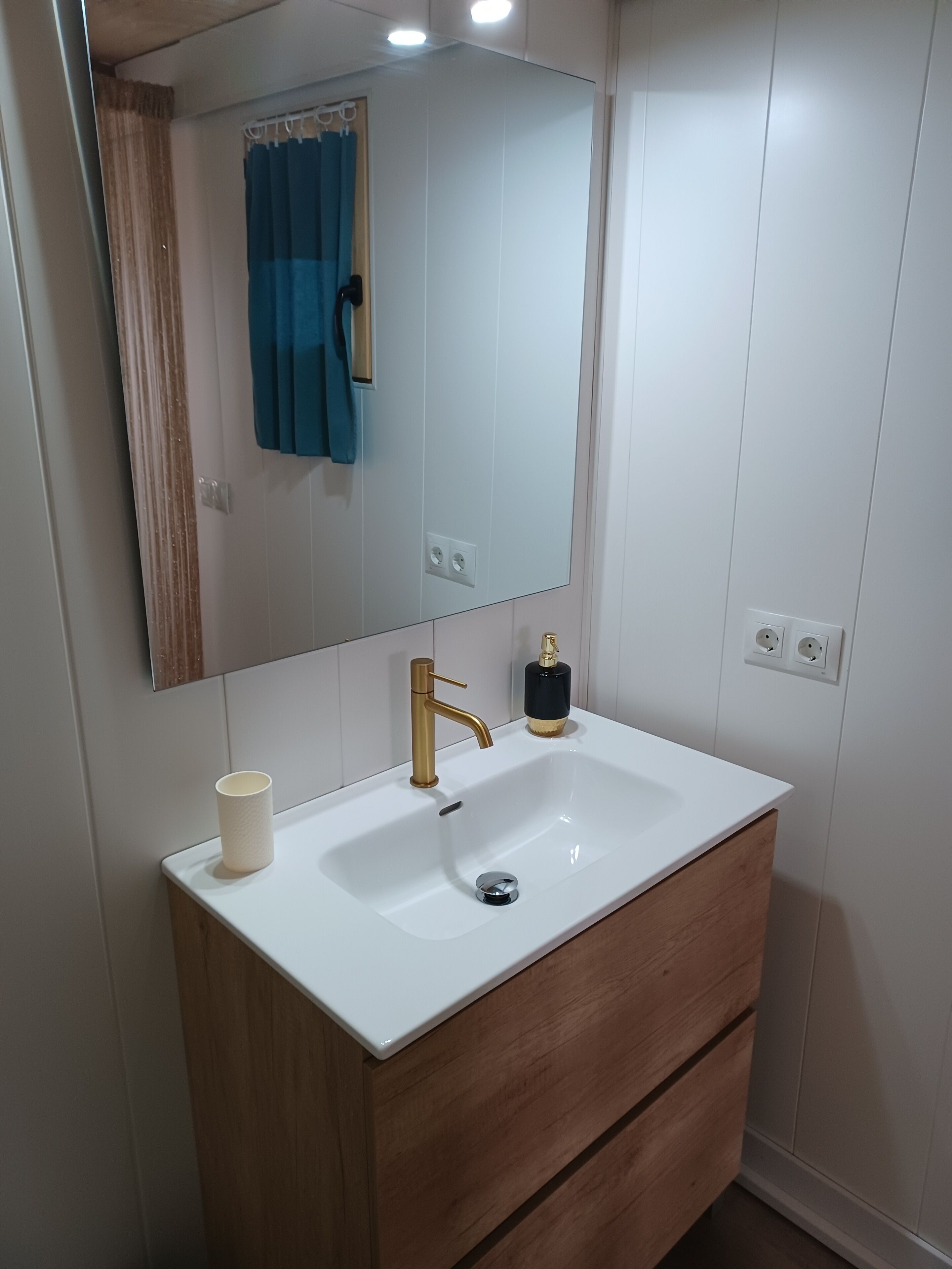 Een badkamer met een wit wastafelmeubel, een gouden kraan en een houten kast.