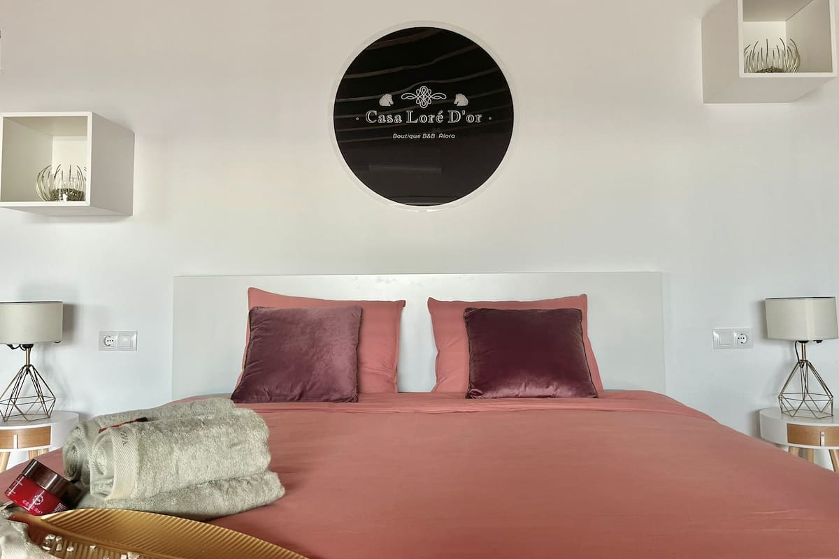 A bedroom with a large bed, two bedside tables with lamps, a round wall decoration, and two small shelves with decorative items.
