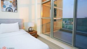 Habitación de hotel con cama, mesita de noche, lámpara y un amplio ventanal con vistas al exterior.