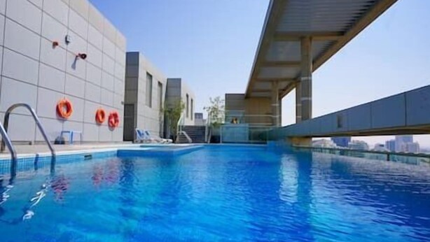 Una piscina con agua azul cristalina, una escalera metálica y dos anillos salvavidas naranja en la pared.