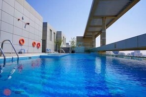 En swimmingpool med klart, blått vatten, en metallstege och två orangefärgade flytringar som hänger på väggen.
