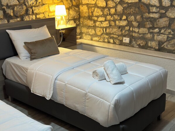 A neatly made bed with a white duvet, a rolled towel, and a lamp on a bedside table. - Te Gjyshi (at Grandfather) (Berat)