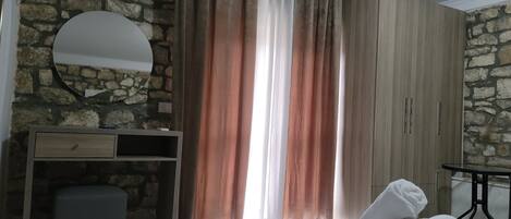 A bedroom with a stone wall, a wooden wardrobe, a bedside table with a towel, and a mirror.