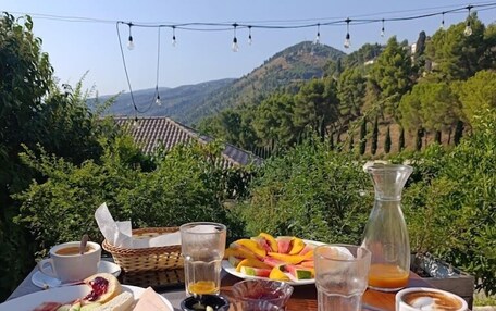 A table set outdoors with a meal consisting of eggs, vegetables, and beverages, overlooking a scenic landscape with hills and vineyards.