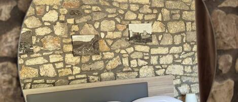 A bedroom with a stone wall, a bed with white bedding, a headboard, and two bedside lamps.