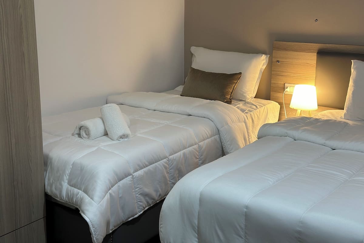 A hotel room with two beds, a wooden headboard, a bedside lamp, and neatly folded towels.