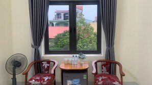 A room with a window, two chairs, a small table, a fan, and a refrigerator. - Sen's homestay (Nam Hoa Lu)