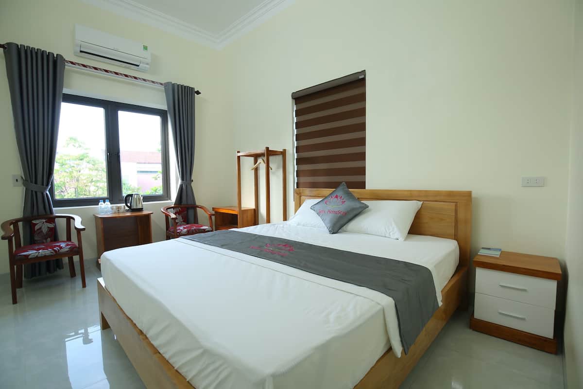 A hotel room with a large bed, a wooden nightstand, a chair, a desk, and a window with curtains.