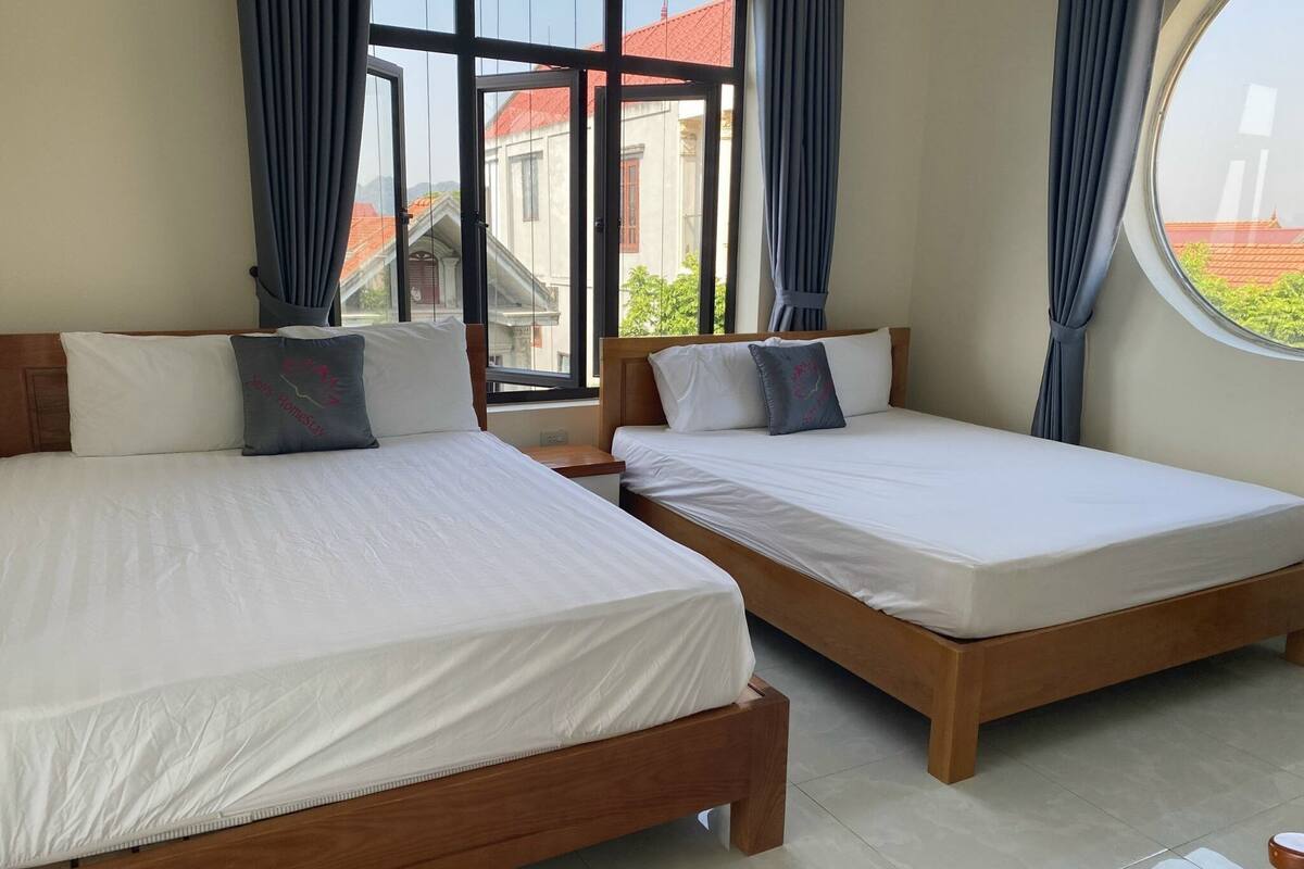 A hotel room with two wooden beds, white bedding, and large windows with curtains.