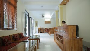 A hotel reception area with a wooden reception desk, seating area with red patterned sofas, and a ceiling fan. - Sen's homestay (Nam Hoa Lu)