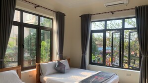 A hotel room with two beds, large windows, an air conditioning unit, and a view of greenery outside. - Sen's homestay (Nam Hoa Lu)