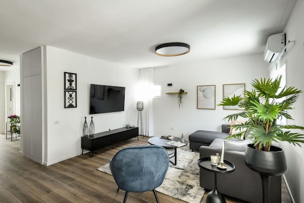 A modern living room with a flat-screen TV, a sofa, a coffee table, and a potted plant.