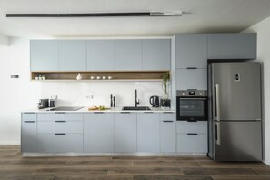 A modern kitchen with grey cabinets, a stainless steel refrigerator, and a built-in oven.