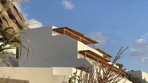 A modern building with a flat roof, a wooden pergola, and a stone wall. - Calistus Mykonos (Mykonos)