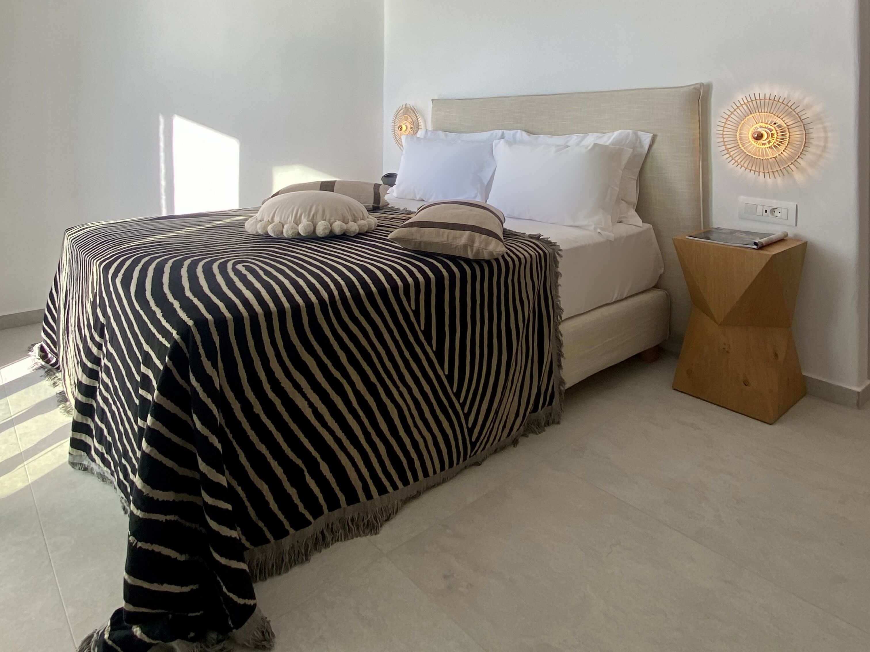 Un dormitorio moderno con una colcha a rayas, una mesita de noche de madera y un aplique en la pared.