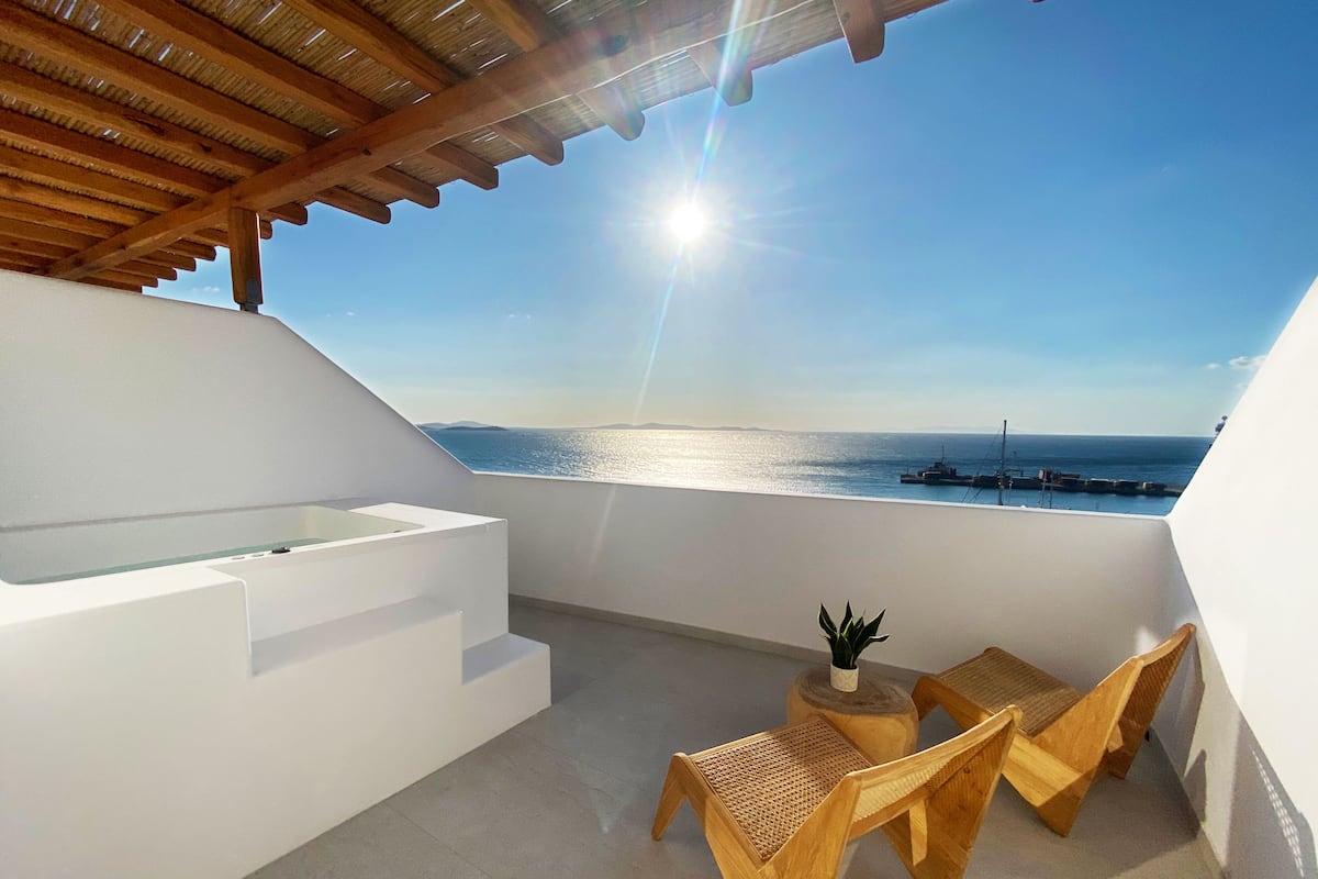 A balcony with a view of the sea, wooden furniture, and a small table with a plant.