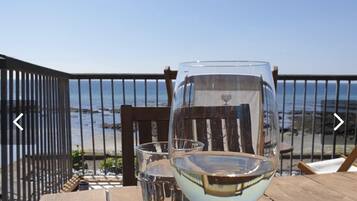 Uma mesa de madeira com dois copos de vinho branco e vista para o oceano.