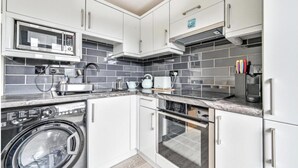 A modern kitchen with white cabinets, a microwave, a kettle, and a washing machine. - Torpoint - Apartment - Sleeps4 - Seaside - Parking (Torpoint)
