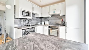 A modern kitchen with white cabinets, a microwave, a kettle, and a built-in oven. - Torpoint - Apartment - Sleeps4 - Seaside - Parking (Torpoint)