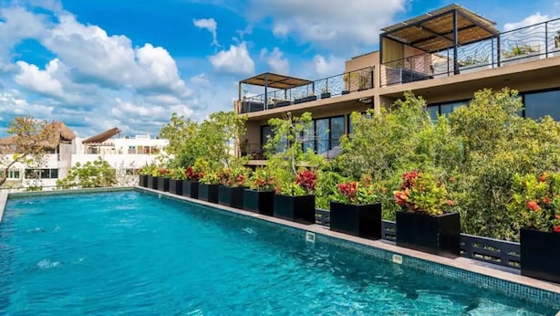 A swimming pool with a clear blue water, surrounded by lush greenery and modern buildings. - Casa Serafin, Beyond Expectations, Beyond Ordinary (Tulum)