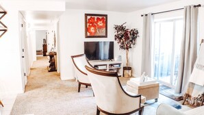Un salon moderne doté d’un téléviseur à écran plat, d’un coin repas avec une table et des chaises, d’une grande fenêtre avec des rideaux et d’un tableau accroché au mur.