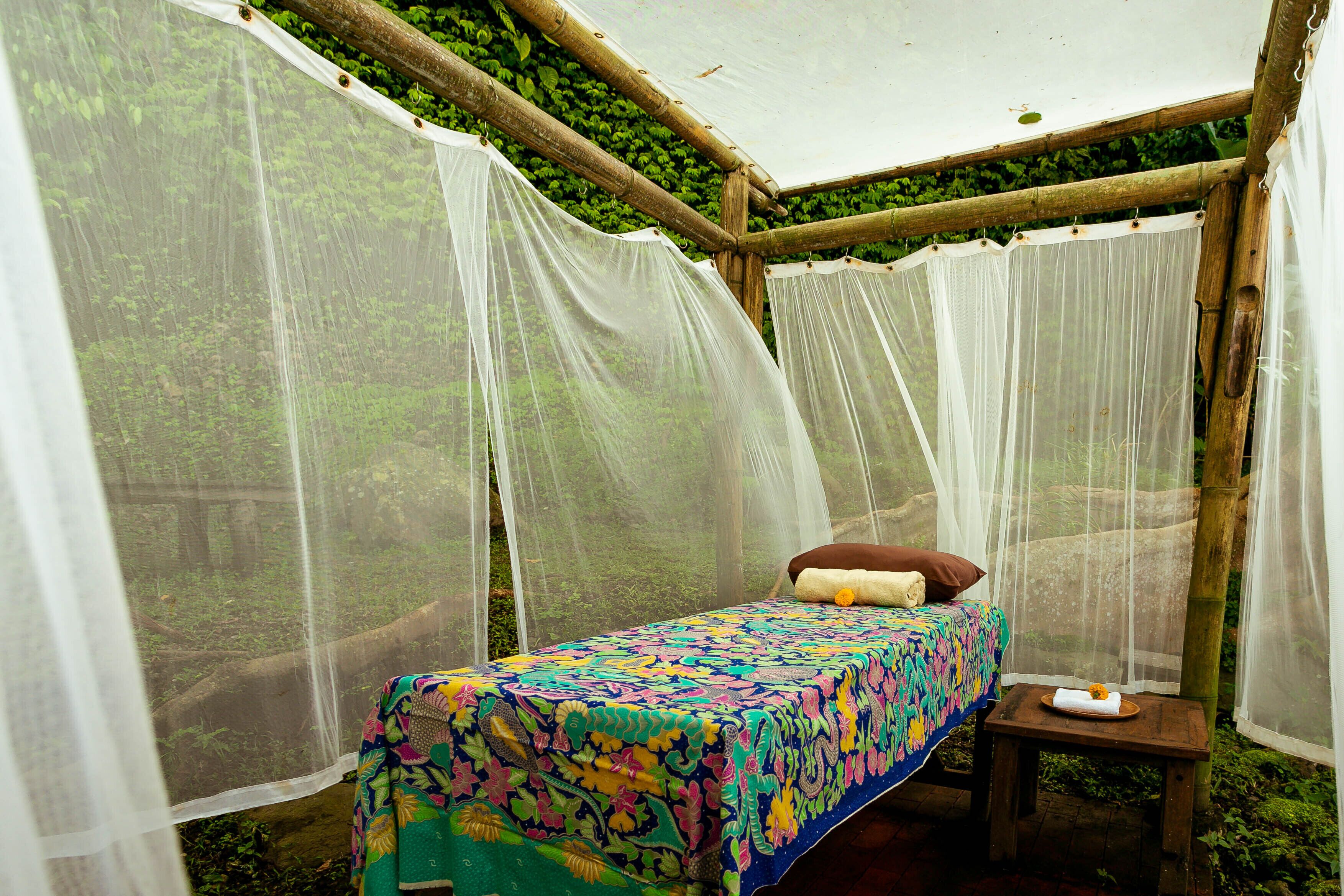 A bed with a colorful bedspread, a small wooden nightstand, and a mosquito netting structure.
