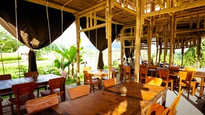 An open-air restaurant with bamboo structures, wooden tables, and chairs, surrounded by lush greenery. - Maha Gangga Valley by ecommerceloka (Karangasem)