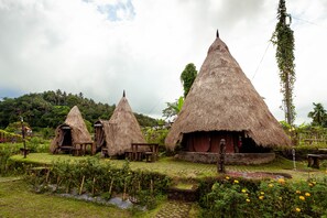 Cabañas de techo de paja, rodeadas de vegetación y un pequeño arroyo.