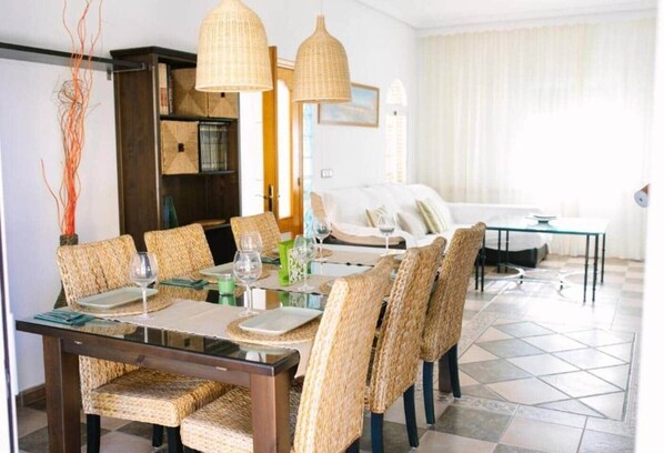 Un espace repas avec une table en verre, des chaises en osier et des luminaires suspendus.