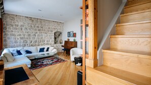 A living room with a stone wall, wooden staircase, white sofa, and a piano. - Secret Orange by DuHomes (Dubrovnik)