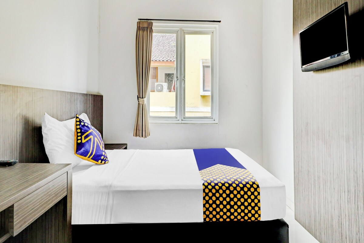 Habitación de hotel con cama, televisor montado en la pared, ventana con cortinas y vistas al exterior.