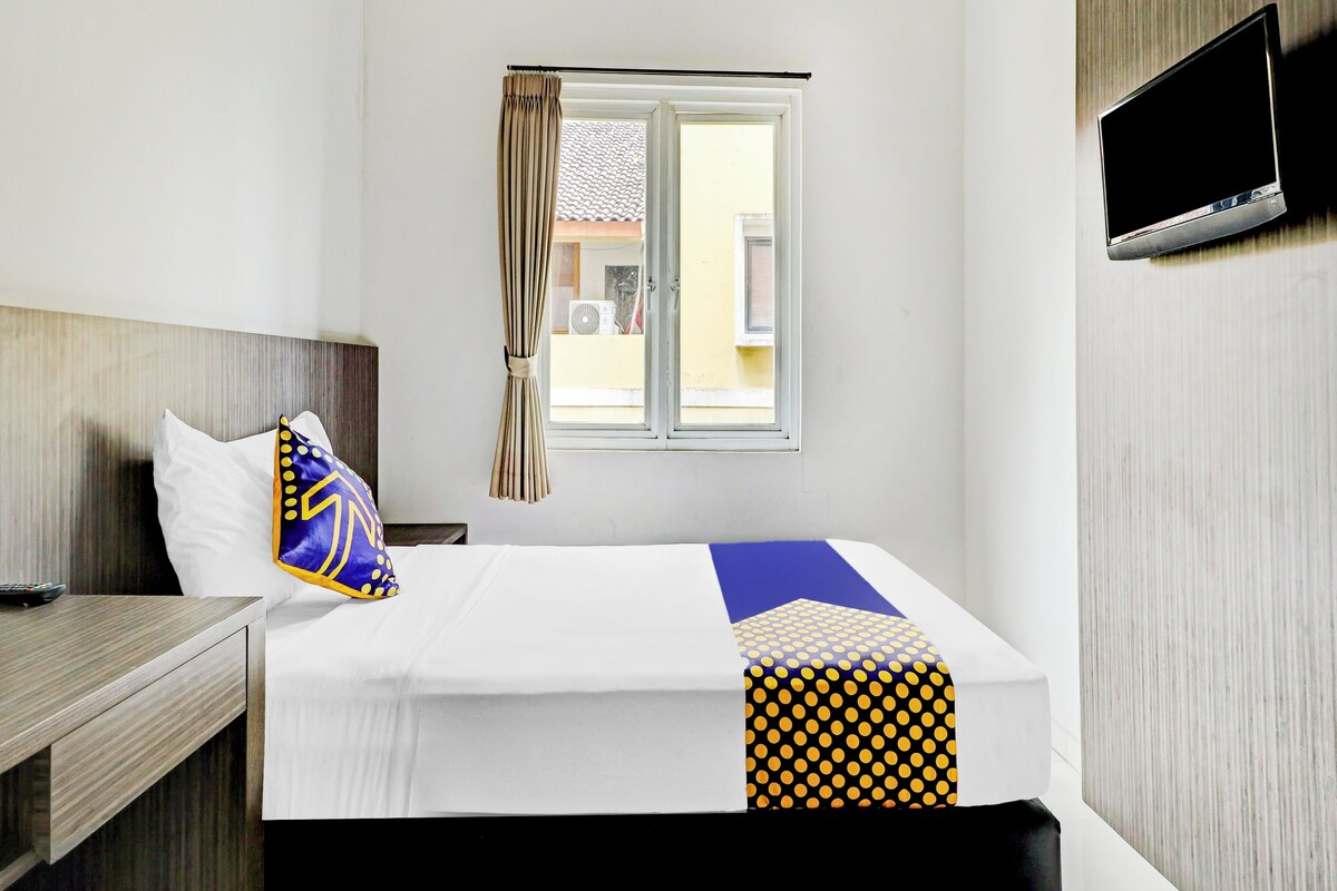 A hotel room with a bed, a TV mounted on the wall, a window with curtains, and a view of the outside.