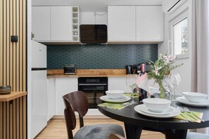 A modern kitchen with white cabinets, a wooden countertop, a black stove, and a dining table set with plates, glasses, and a vase of flowers. - Cozy Apartment in the Center | Workplace | For 6 People (Wroclaw)