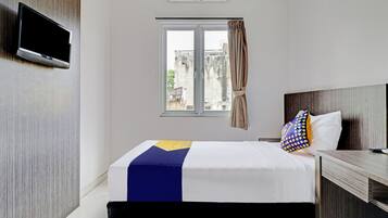 Een hotelkamer met een bed, een aan de muur bevestigde televisie, een raam met gordijnen en een uitzicht op gebouwen.