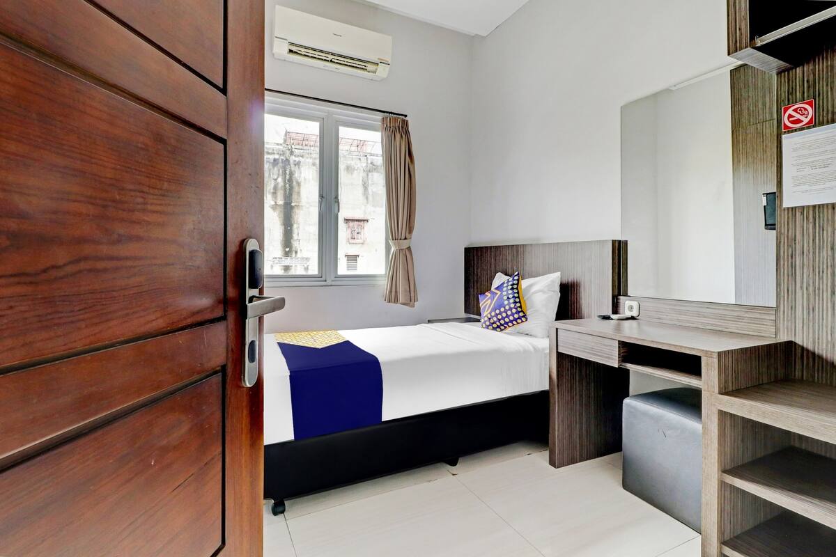 Une chambre d’hôtel avec un lit, un bureau, une armoire et une fenêtre avec des rideaux.