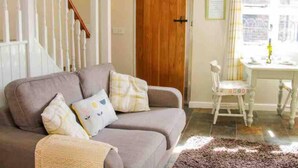 A living room with a grey sofa, a wooden door, a dining table with chairs, and a staircase. - Cottagesleeps2-fireplace-valleyview-patio-garden (Telford)