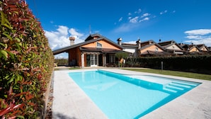 Ein Wohnhaus mit Schwimmbad, einem gepflegten Garten und wolkenlosem, blauem Himmel.